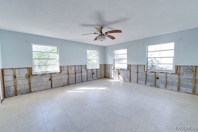 empty room featuring a textured ceiling, ceiling fan, and tile walls