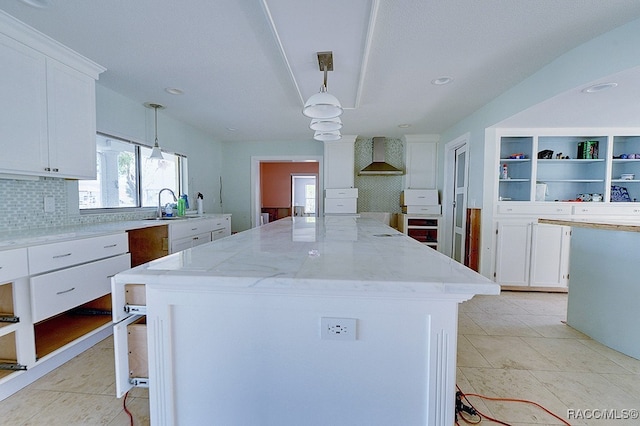 kitchen featuring white cabinets, a center island, wall chimney range hood, and hanging light fixtures