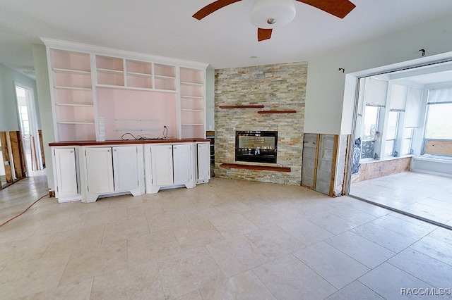 unfurnished living room with light tile patterned flooring, a stone fireplace, and built in features