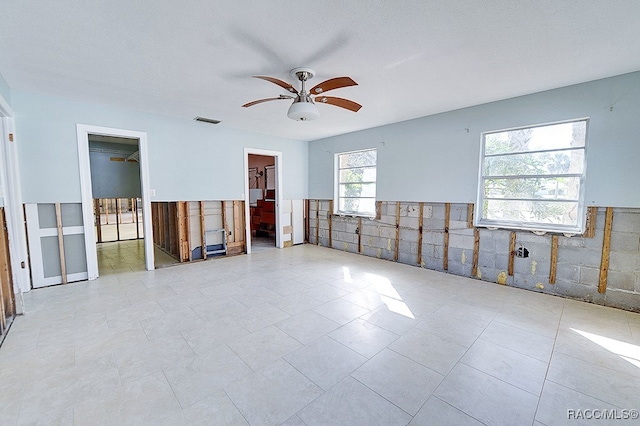 empty room with ceiling fan, light tile patterned flooring, and tile walls