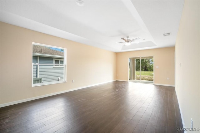 unfurnished room featuring a raised ceiling, visible vents, dark wood-type flooring, a ceiling fan, and baseboards