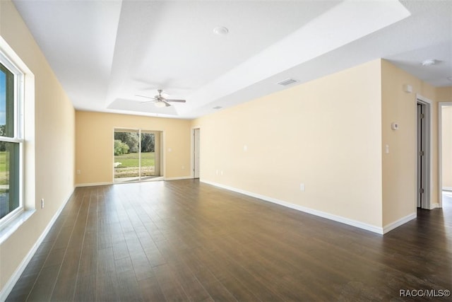 empty room with baseboards, visible vents, a raised ceiling, and dark wood finished floors