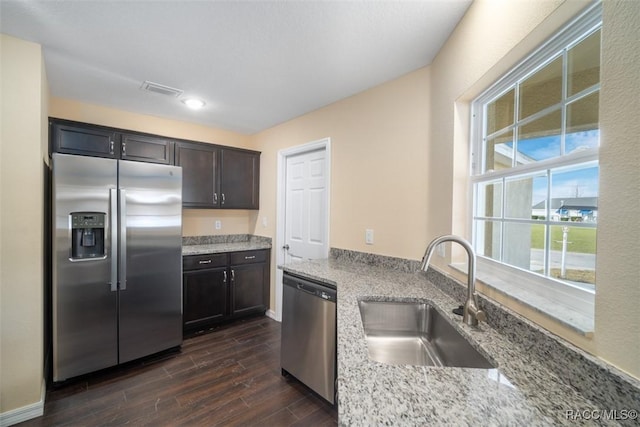 kitchen featuring appliances with stainless steel finishes, dark wood finished floors, a sink, and light stone countertops