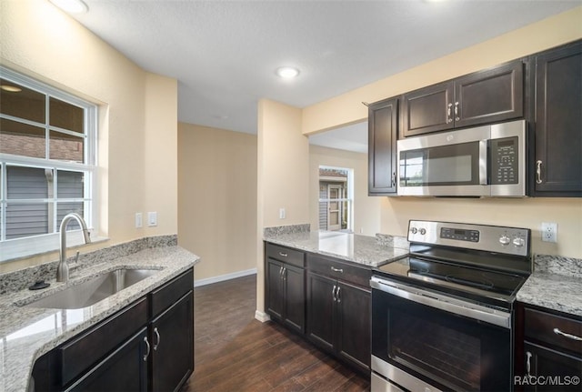 kitchen featuring baseboards, dark wood finished floors, light stone countertops, stainless steel appliances, and a sink