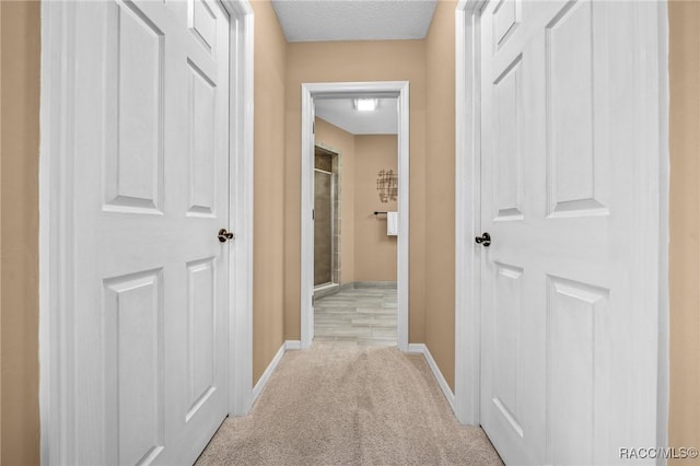 hallway featuring baseboards, light colored carpet, and a textured ceiling