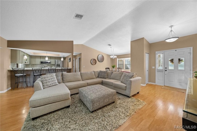 living room featuring visible vents, a textured ceiling, light wood-type flooring, and vaulted ceiling