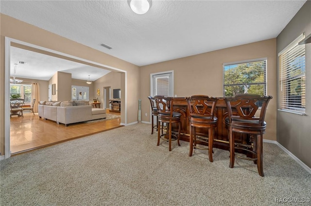 carpeted dining room featuring a dry bar, a notable chandelier, baseboards, and a textured ceiling