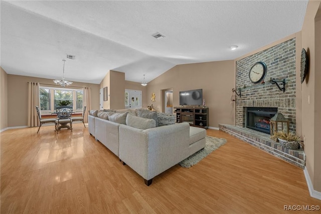 living area with visible vents, a brick fireplace, lofted ceiling, light wood-style flooring, and an inviting chandelier