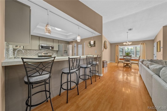 kitchen featuring gray cabinets, backsplash, stainless steel appliances, light wood finished floors, and a raised ceiling