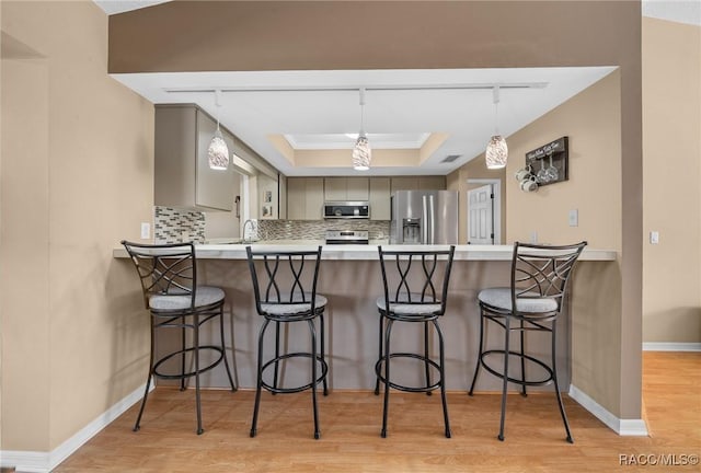 kitchen featuring a tray ceiling, tasteful backsplash, light wood-style floors, appliances with stainless steel finishes, and a peninsula