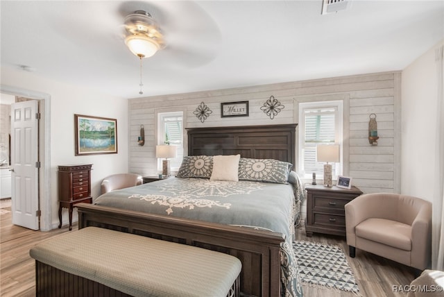 bedroom with ceiling fan, light hardwood / wood-style floors, and wood walls