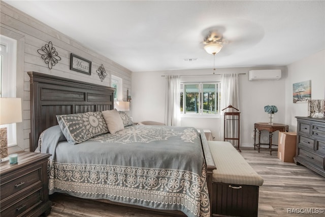 bedroom with light wood-type flooring, an AC wall unit, ceiling fan, and wood walls