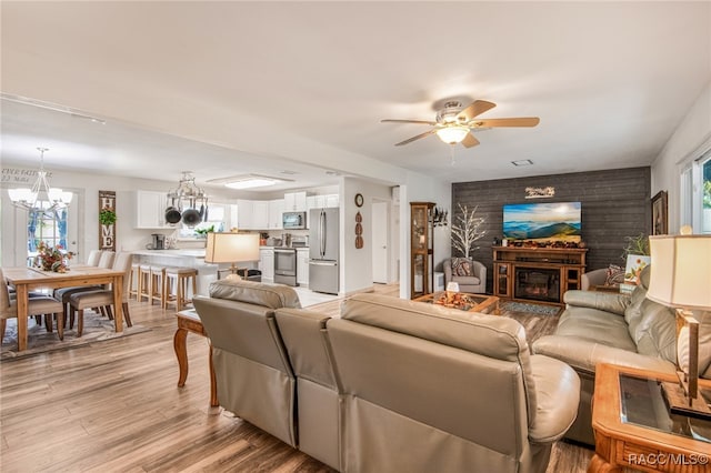 living room featuring a fireplace, light hardwood / wood-style floors, and ceiling fan with notable chandelier