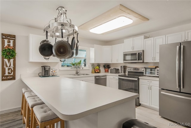 kitchen with a kitchen breakfast bar, light wood-type flooring, stainless steel appliances, sink, and white cabinets