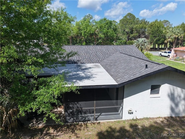 view of home's exterior with stucco siding, a sunroom, and roof with shingles