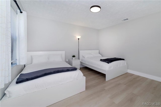 bedroom with visible vents, baseboards, a textured ceiling, and wood finished floors