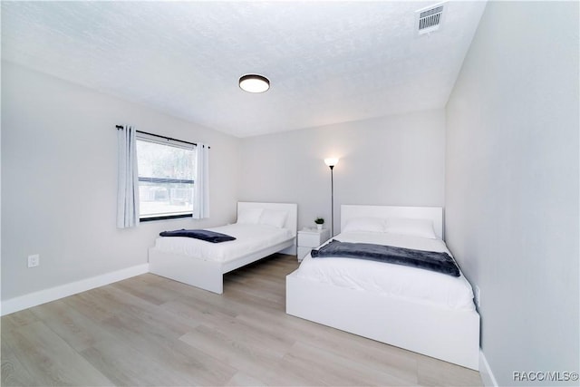 unfurnished bedroom with a textured ceiling, wood finished floors, baseboards, and visible vents