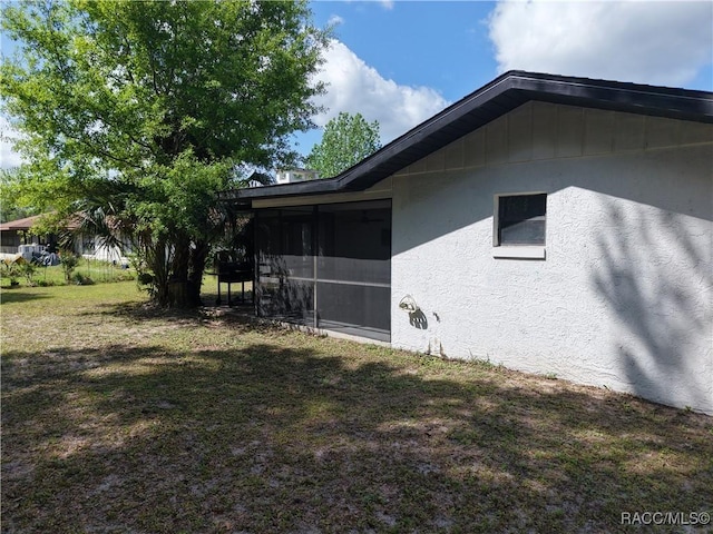 view of side of home featuring stucco siding, a sunroom, and a lawn