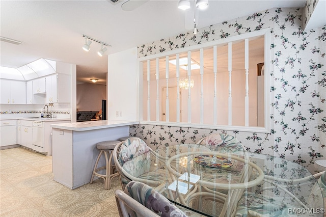 kitchen with kitchen peninsula, a kitchen breakfast bar, rail lighting, sink, and white cabinetry