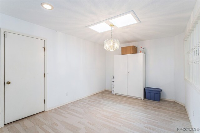 empty room featuring a notable chandelier, light wood-type flooring, and a skylight