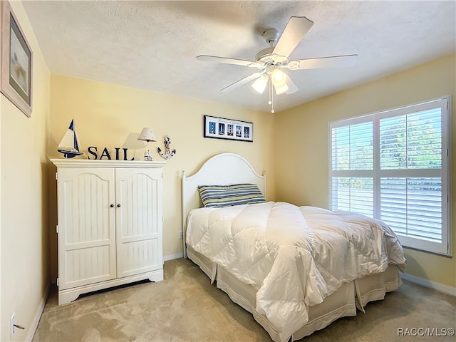 bedroom featuring ceiling fan, light carpet, and a textured ceiling