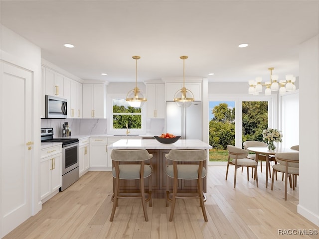 kitchen with appliances with stainless steel finishes, decorative light fixtures, light hardwood / wood-style flooring, white cabinets, and a kitchen island