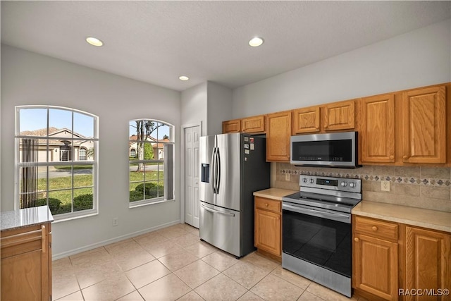 kitchen featuring stainless steel appliances, a wealth of natural light, tasteful backsplash, and light tile patterned flooring