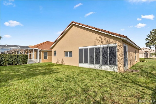 back of property with glass enclosure and a lawn