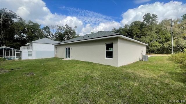 back of property featuring a shingled roof, central air condition unit, a lawn, and stucco siding