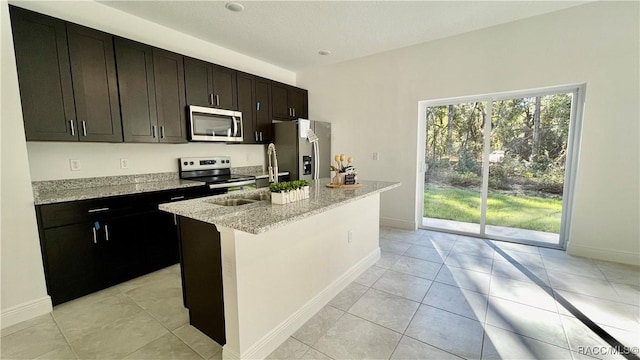 kitchen with a center island with sink, light stone counters, stainless steel appliances, and a sink