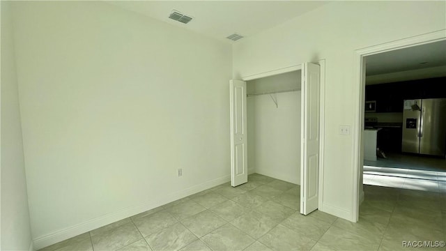 unfurnished bedroom with a closet, stainless steel fridge, visible vents, and baseboards