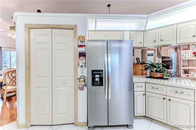 kitchen featuring light tile patterned floors, tile counters, ceiling fan, and stainless steel refrigerator with ice dispenser