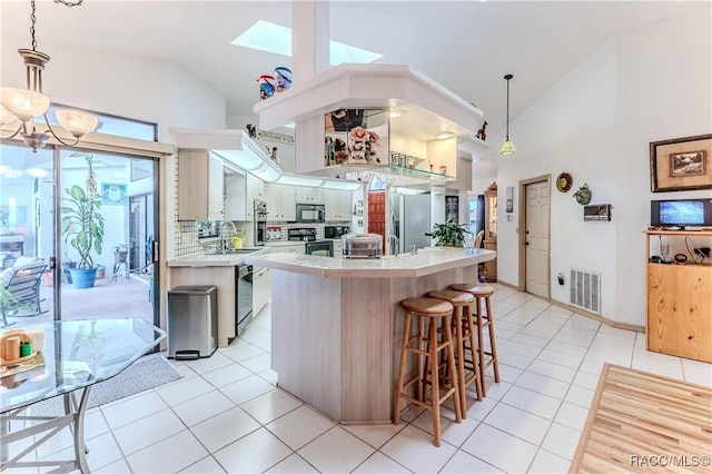 kitchen featuring light tile patterned flooring, high vaulted ceiling, hanging light fixtures, a kitchen island, and black appliances