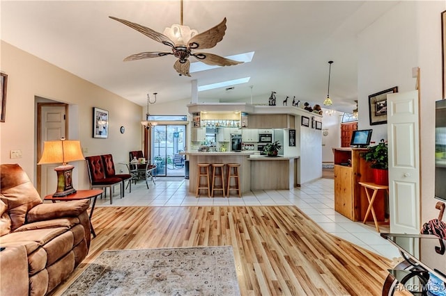 living room with ceiling fan, lofted ceiling with skylight, and light tile patterned floors