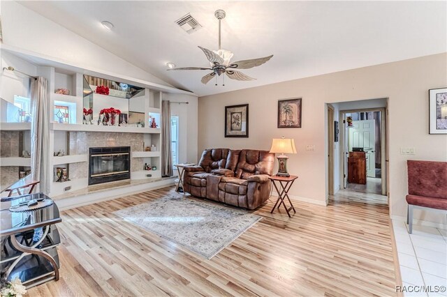 living room with lofted ceiling, built in shelves, ceiling fan, and light wood-type flooring