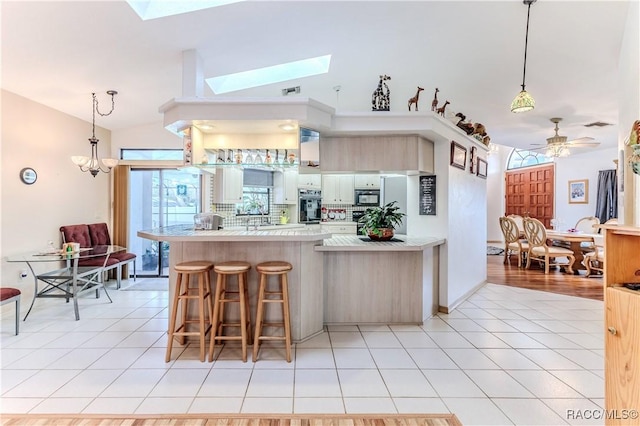 kitchen featuring lofted ceiling with skylight, black appliances, a kitchen bar, light tile patterned floors, and kitchen peninsula