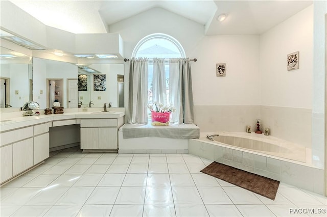 bathroom with tile patterned floors, vaulted ceiling, vanity, and tiled tub