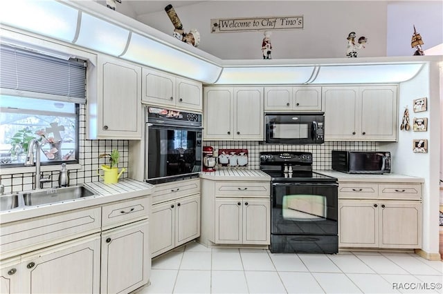 kitchen with sink, light tile patterned floors, tasteful backsplash, black appliances, and tile countertops