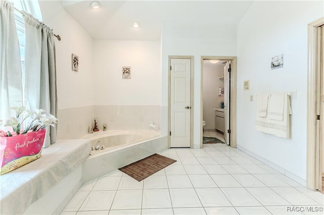 bathroom with tiled tub, tile patterned floors, toilet, and plenty of natural light