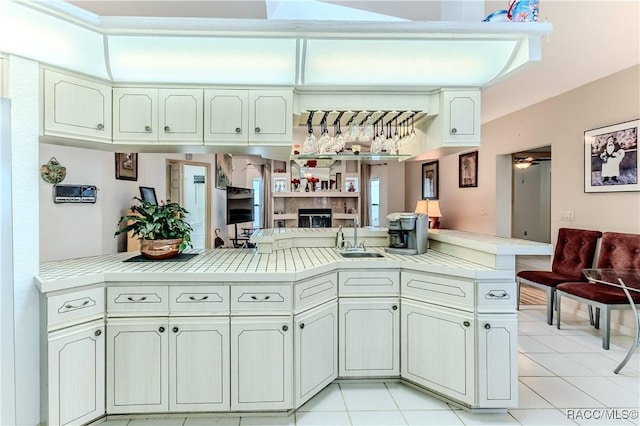 kitchen with tile countertops, sink, light tile patterned floors, ceiling fan, and kitchen peninsula