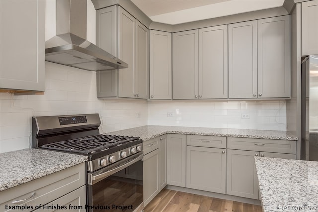 kitchen with wall chimney exhaust hood, stainless steel gas stove, light stone counters, and light hardwood / wood-style flooring