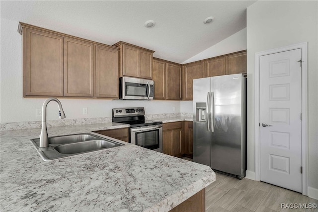 kitchen with vaulted ceiling, appliances with stainless steel finishes, kitchen peninsula, and sink