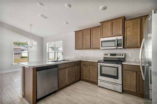 kitchen with vaulted ceiling, appliances with stainless steel finishes, pendant lighting, sink, and kitchen peninsula