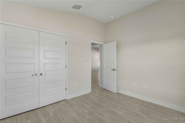 unfurnished bedroom featuring light hardwood / wood-style flooring, a closet, and vaulted ceiling