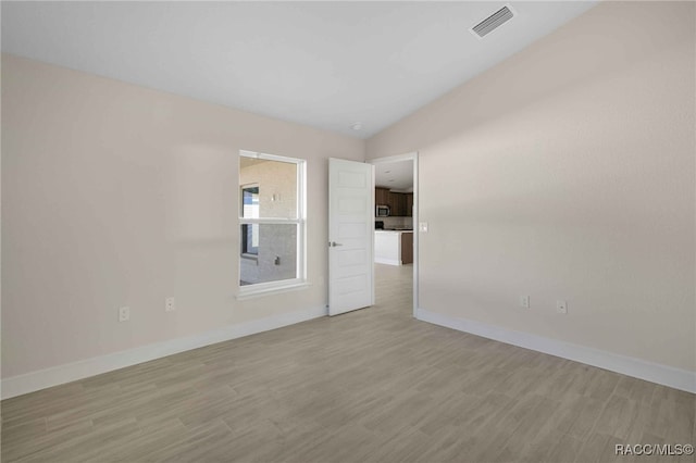 unfurnished room featuring lofted ceiling and light hardwood / wood-style flooring