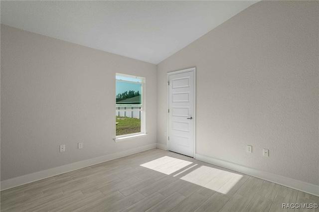 empty room featuring vaulted ceiling and light wood-type flooring