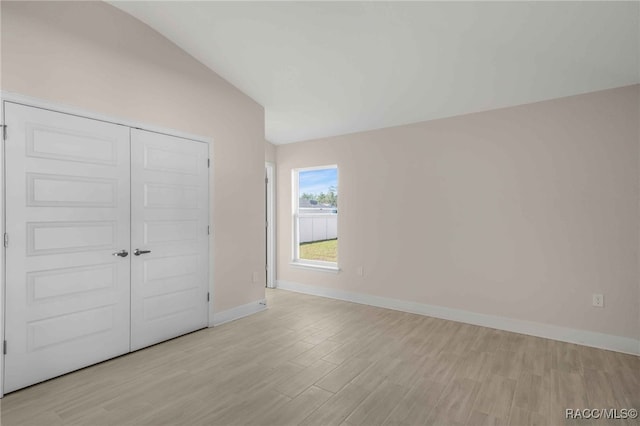 unfurnished bedroom featuring lofted ceiling, light wood-type flooring, and a closet