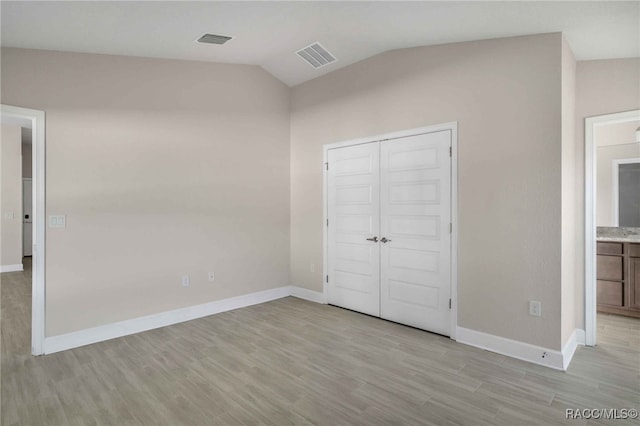 unfurnished bedroom featuring vaulted ceiling, light wood-type flooring, and a closet