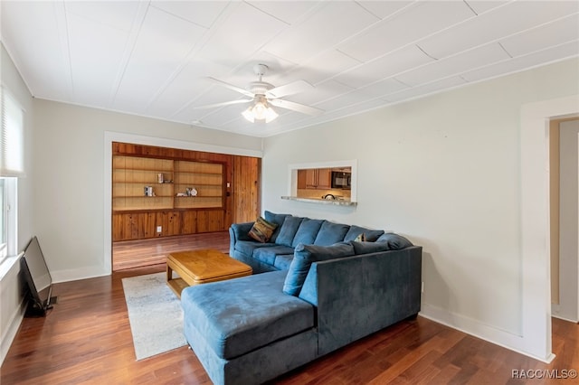 living room with built in shelves, dark hardwood / wood-style floors, and ceiling fan