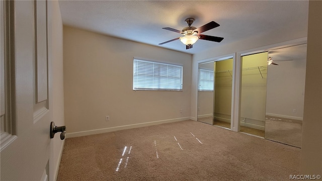 unfurnished bedroom with ceiling fan, carpet floors, a textured ceiling, and multiple closets